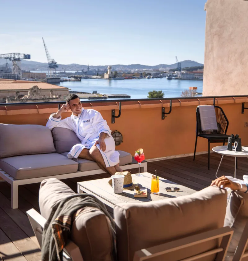 Personnes en peignoirs sur une terrasse avec vue mer.